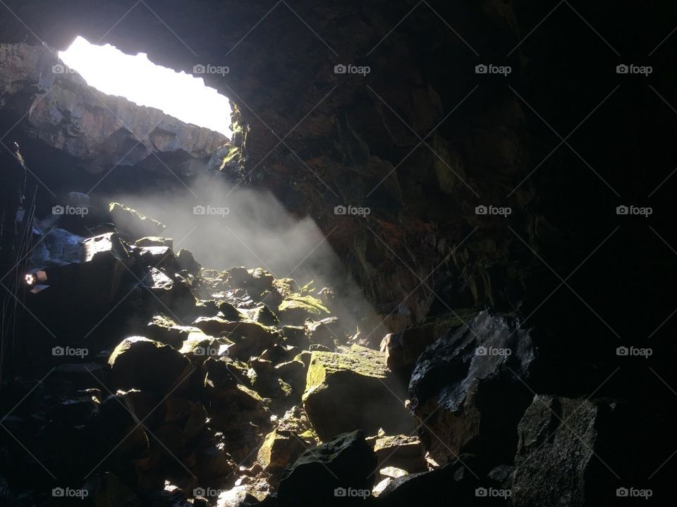 Sunlight comes through a hole in the roof of the cave and shows moss covered rocks 