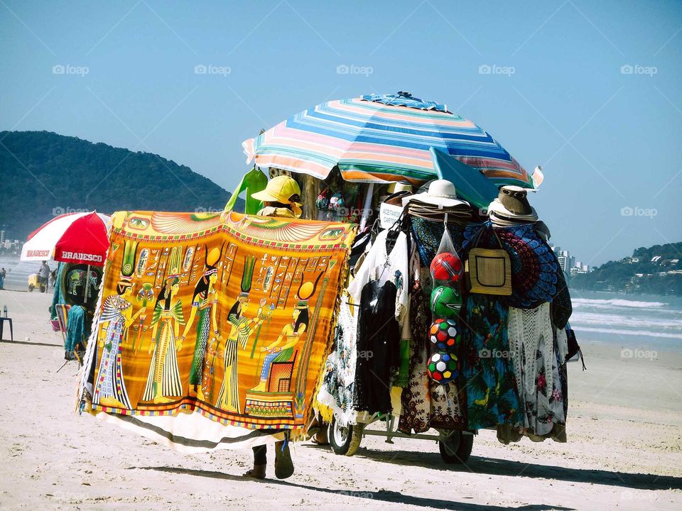 Beautiful Brazilian Beach, at Guarujá's Enseada Beach, sunny day . There's a Man with a cart, a shop cart, selling clothes, balls and umbrellas.