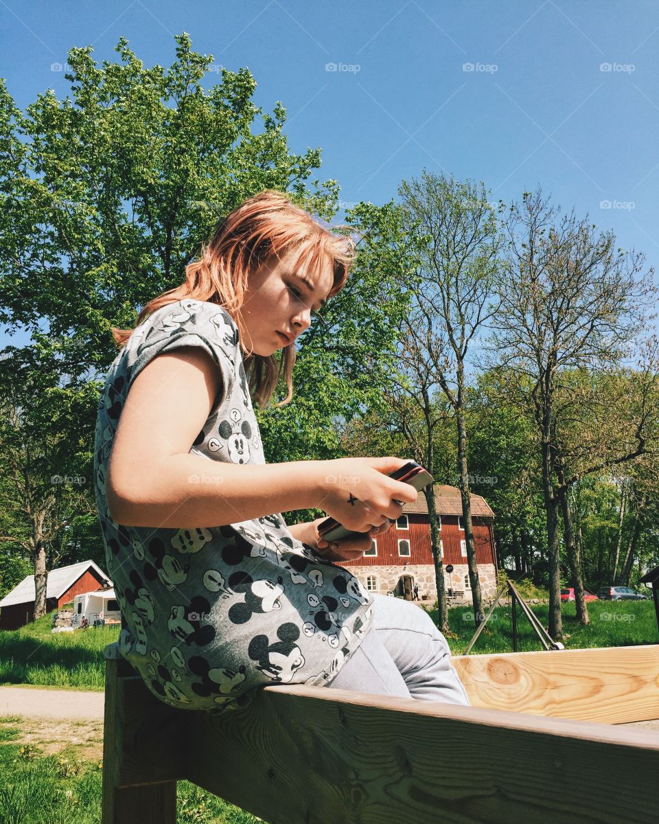 Girl using her phone sitting on the fence