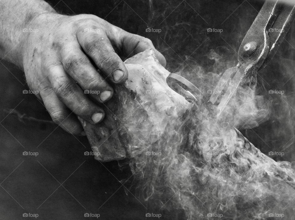 Monochrome hard working hands of a blacksmith applying bees wax to finish a piece of forged metal 