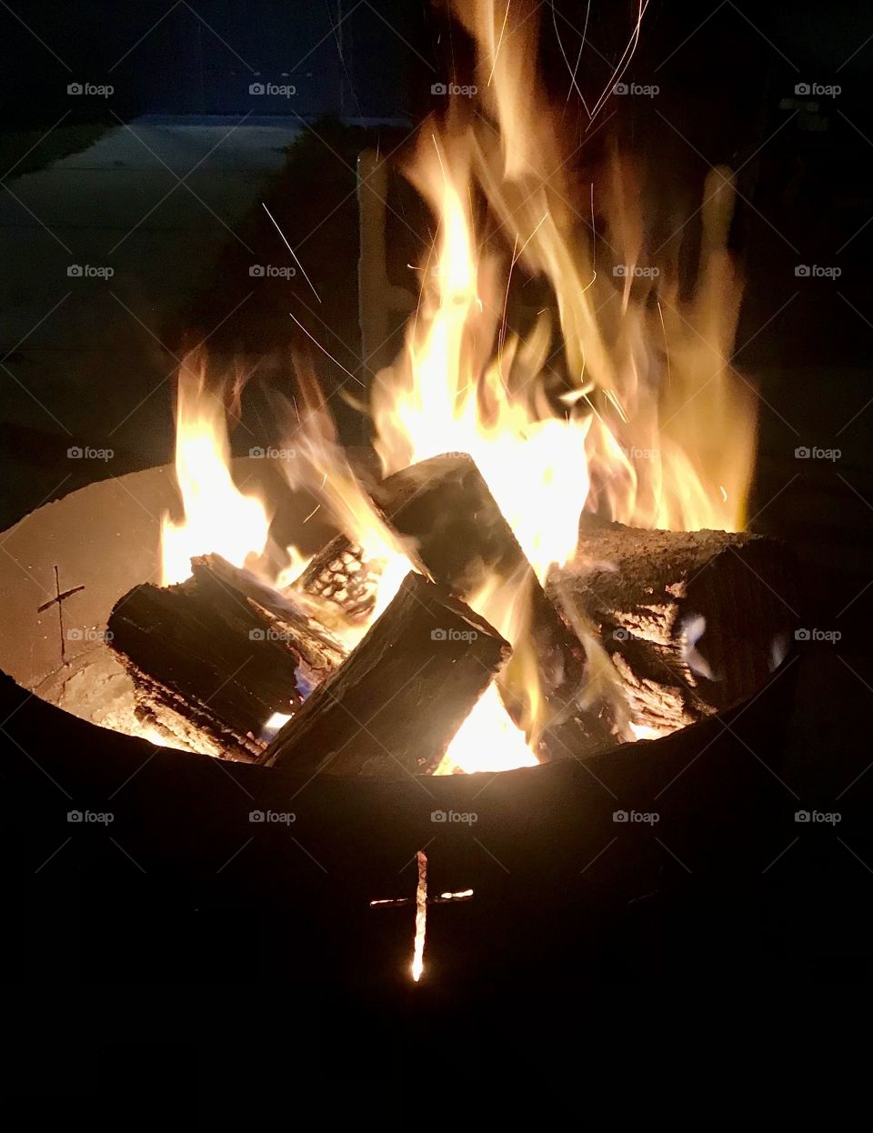 A bright wood fire burning in a container with a cross carved into it at nighttime 