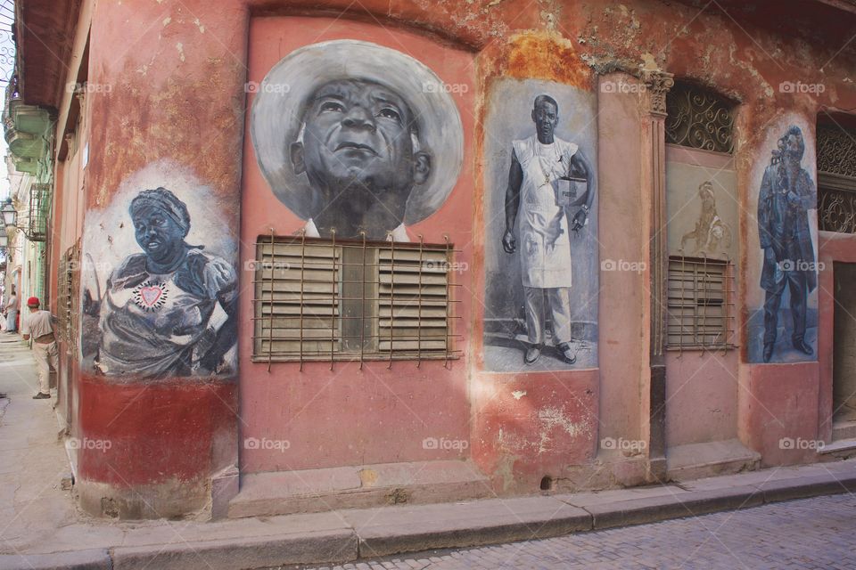 In Old Havana, Cuba, a worn building has individual painted murals of people.