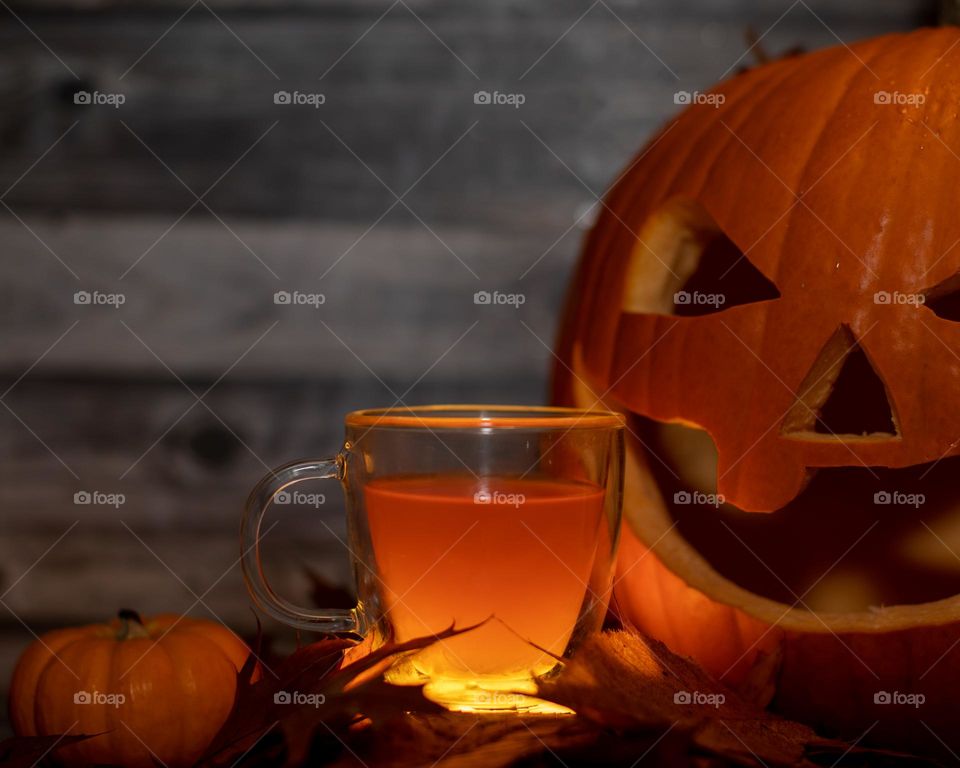 A glowing glass of cider with autumn leaves and pumpkins