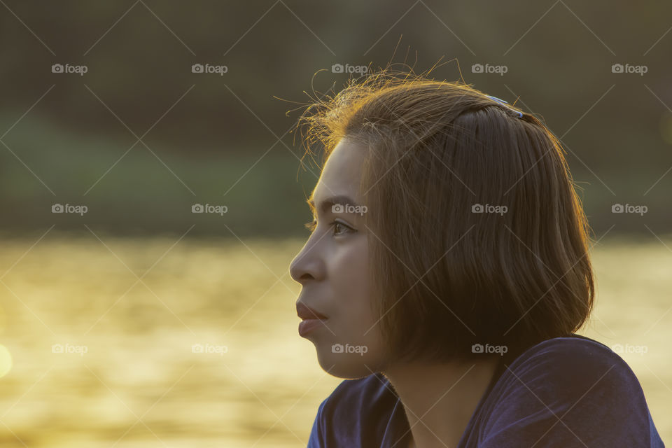 Portrait of Asian woman sitting by the river and the reflected light gold in water.