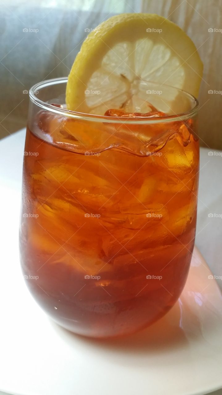 A glass of Lemon Iced Tea topped with a add sliced of lemon