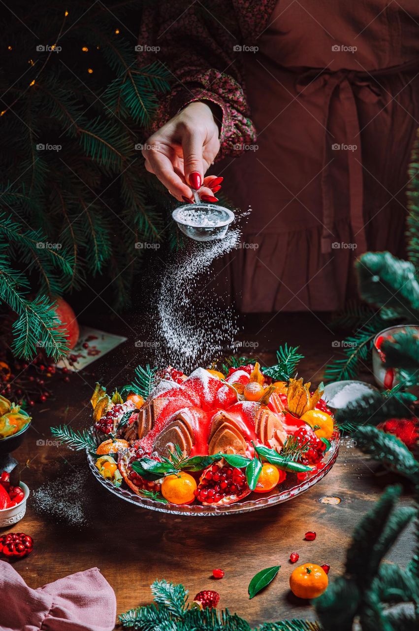 Christmas table setting. Bundt cake pudding sprinkled with sugar powder decorated with pomegranate and tangerines. High quality photo