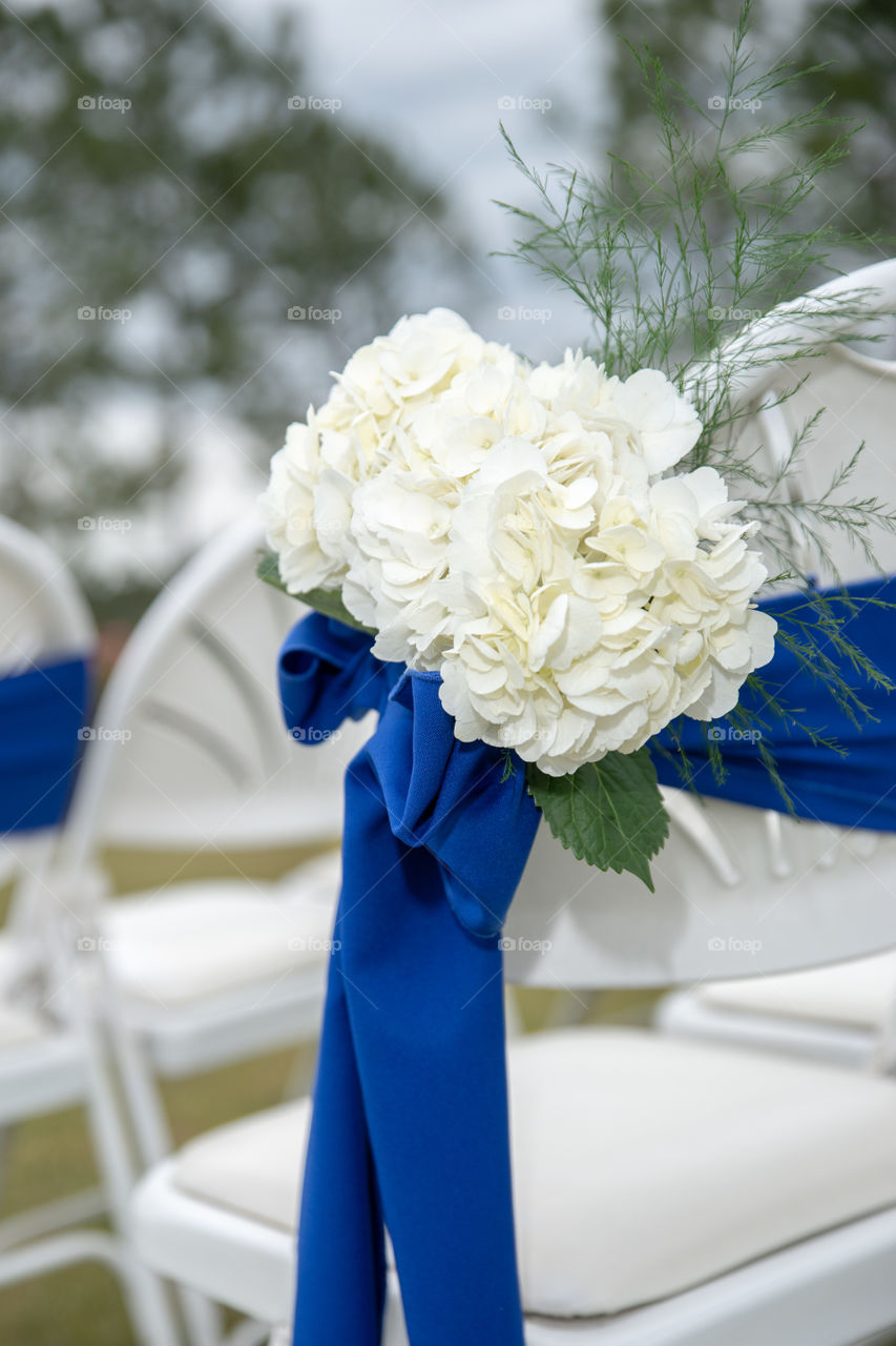 white wedding ceremony chairs with blue bows and ribbons and white flowers