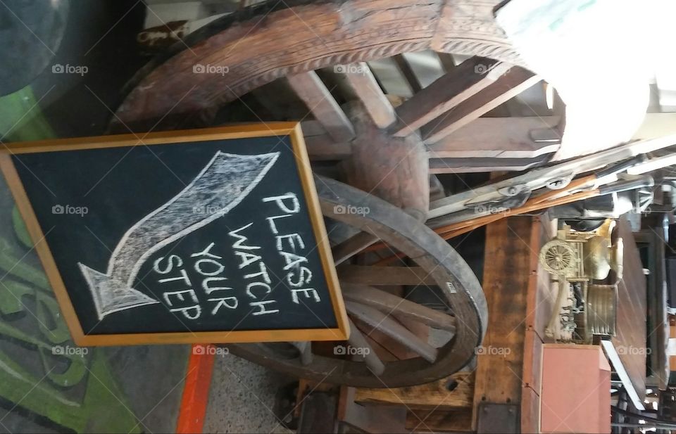 A Watch your step sign is leaned on  vintage Antique wheels made out of wood
