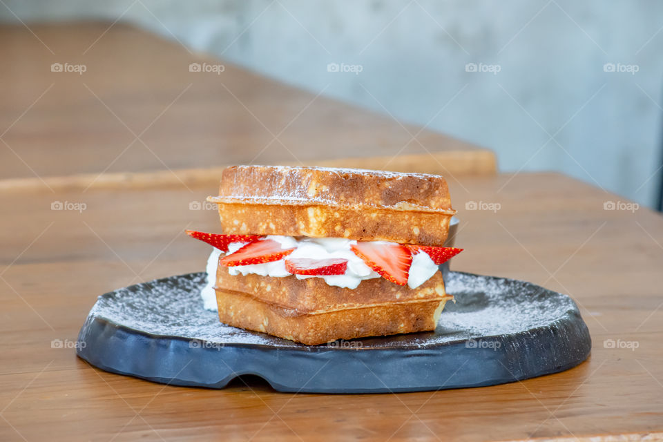 Waffle Strawerry fresh cream in the black plate on wooden table.