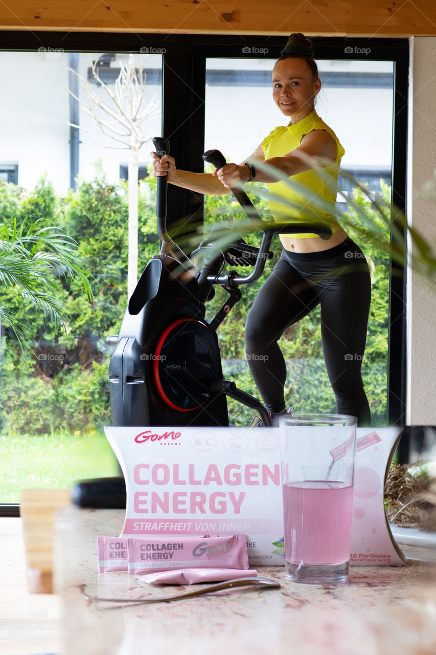 Female between 30 and 40 years old is making cardio. Glass of GOMO collagen, secomdary packaging, and collagen energy sticks in the background.