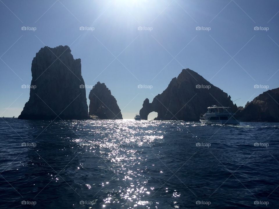 Shimmering blue reflective ocean on a bright, sunny day in Cabo San Lucas in the Mexican Riviera with rocky cliffs and a boat in the distance and clear skies