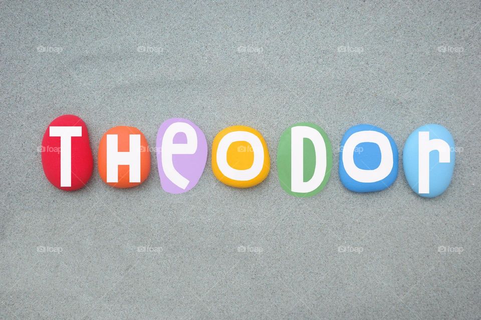 Theodor, masculine given name composed with multi colored hand painted stone letters over green sand