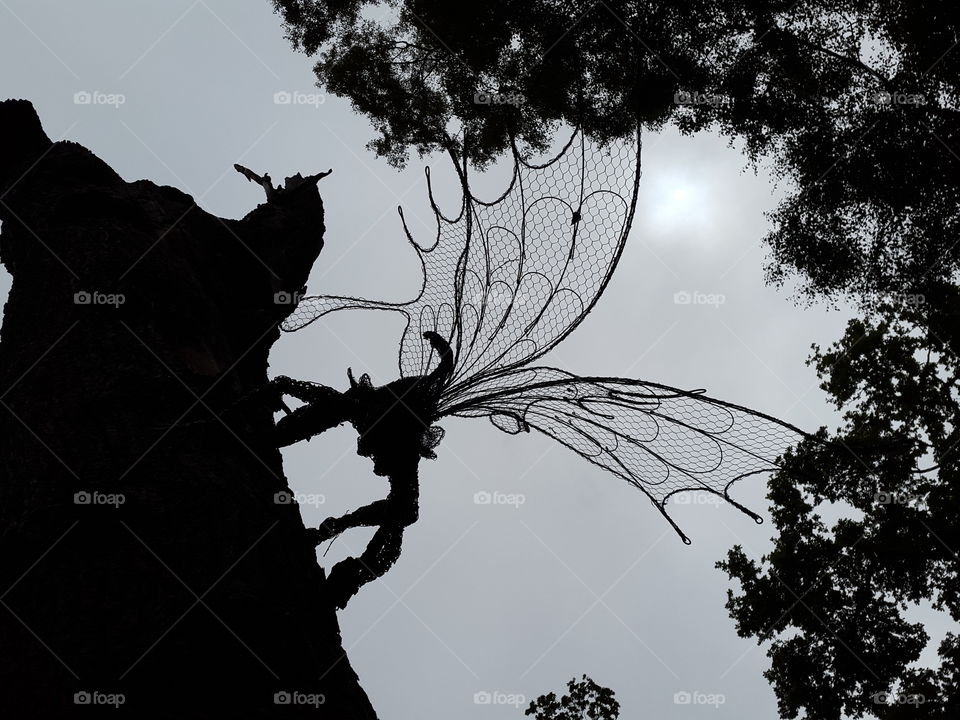 Wire sculpted fairy on tree trunk contrasted by dark skys