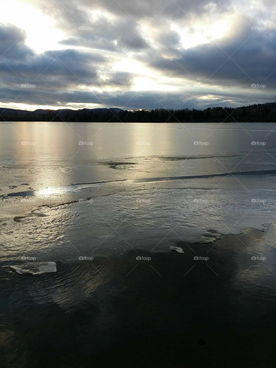 View of a lake covered with ice at sundown with mountains