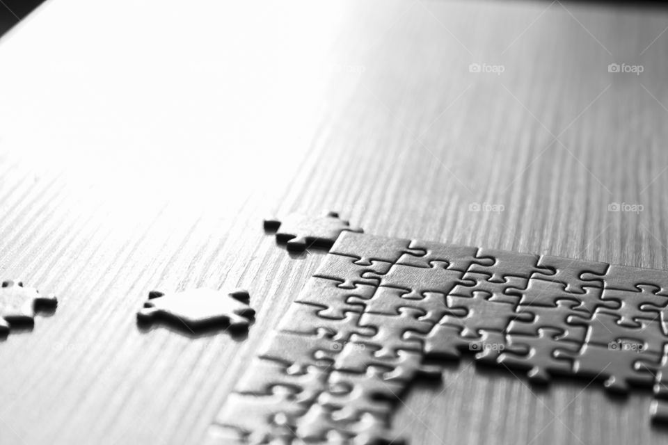 An unfinished puzzle lying on a wooden table with some left over pieces in Black and White.