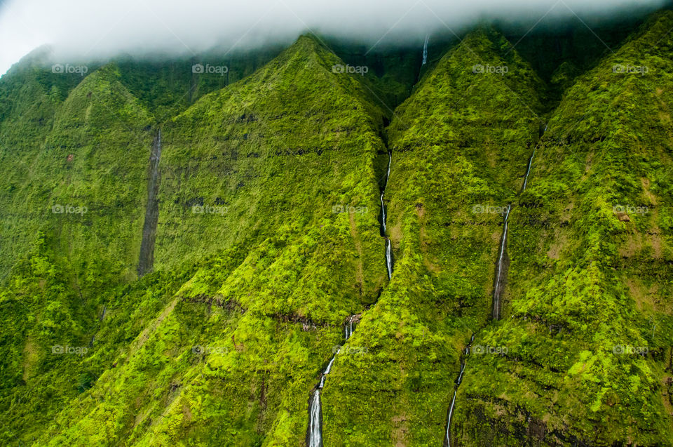 Aerial view of mountainside with multiple waterfalls in Hawaii.