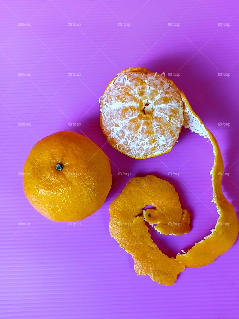 A whole Mandarin Orange and a half peeled Mandarin Orange on pink background.
