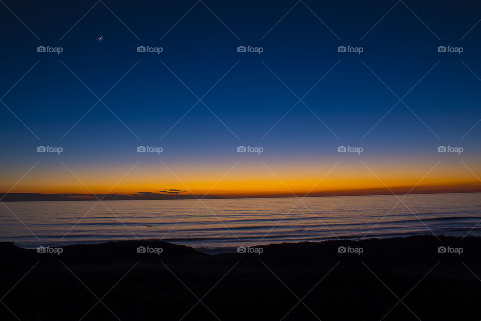The Moon chasing the Sun over the horizon.