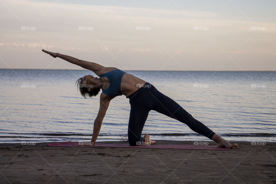Girl practices yoga on the seashore at sunset in summer