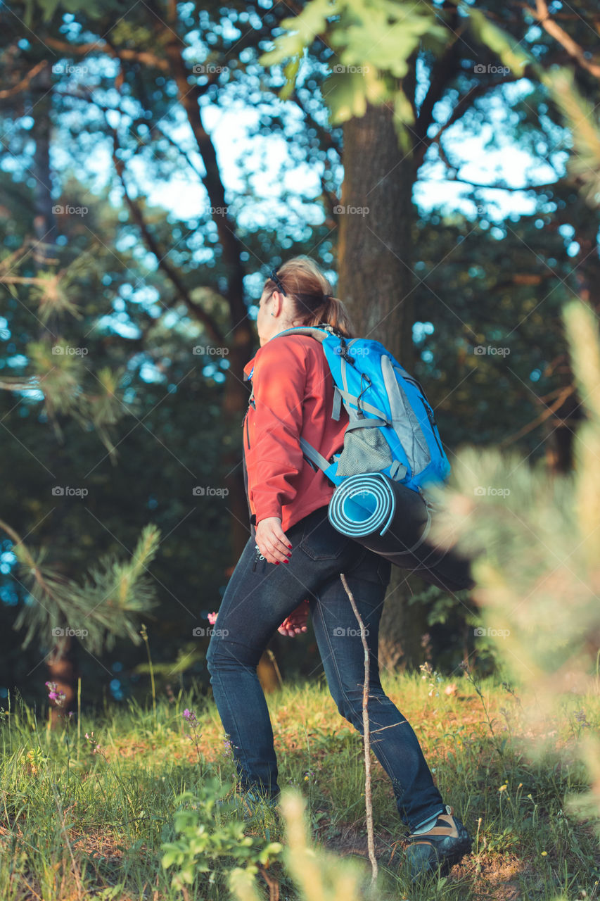 Young woman hiker with backpack walking along the path through the forest during summer vacation trip