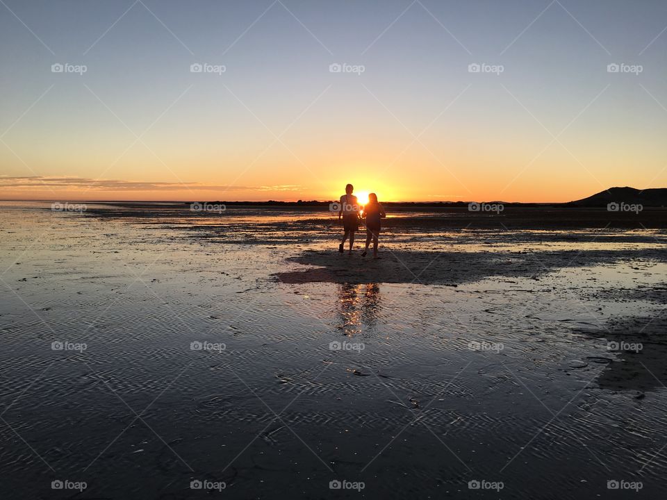 Remote beach at sunset, silhouette of couple in far distance 