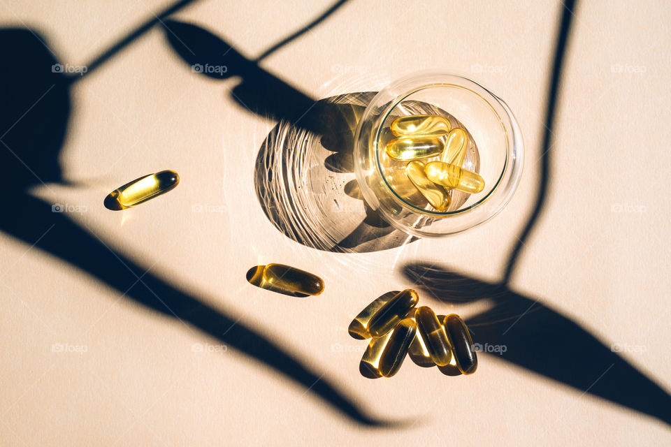 Capsules with omega-3 oil in glass cup with the shadow from monstera leaves 