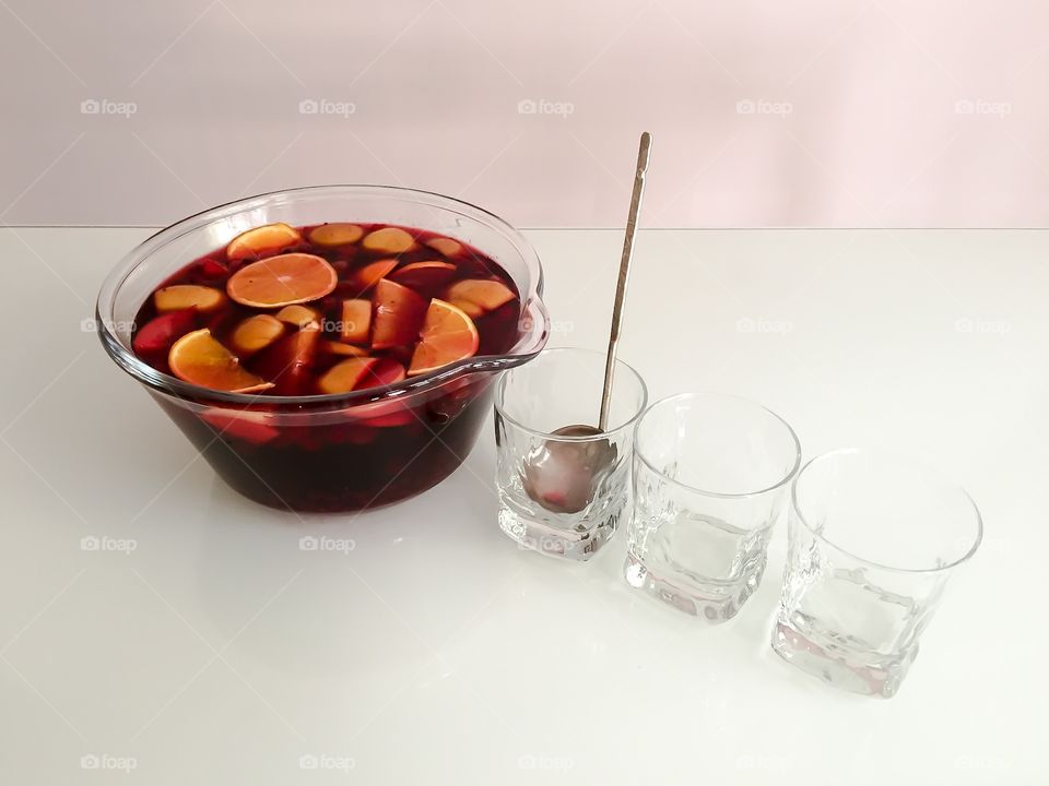 A bowl of fruit beverage and glasses with ladle