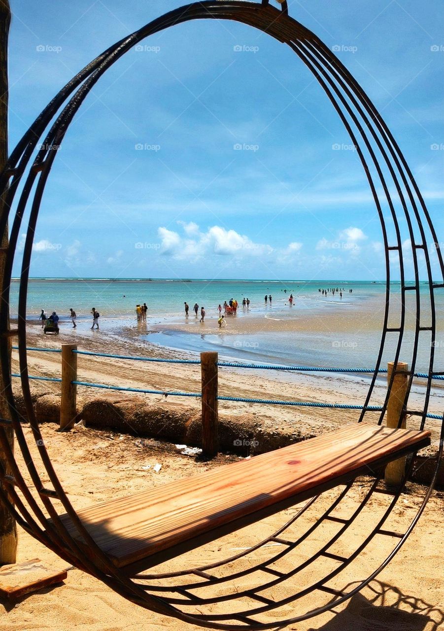 circular iron swing with wooden seat on the shore of Maceió -Alagoas Brazil.  This is an instagrammable swing much used by tourists, it has the beautiful Ponta Verde beach in the background.