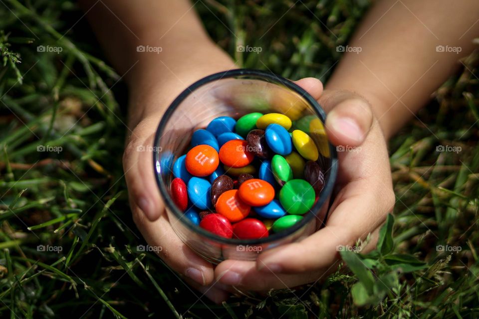 Child's hands are holding candies in a transparent glass