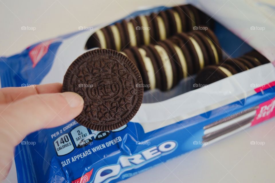 A persons hand taking an Oreo from an open package with a white background