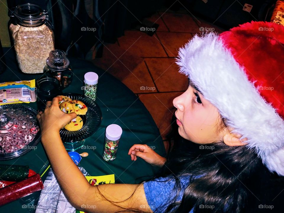 little girl in santa hat stealing a cookie looking over shoulder when caught