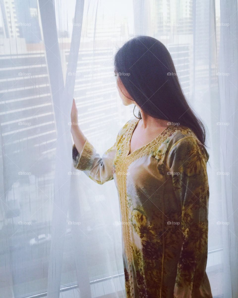 Girl looking out on Abu Dhabi city reflecting during Ramadan month in traditional clothing 