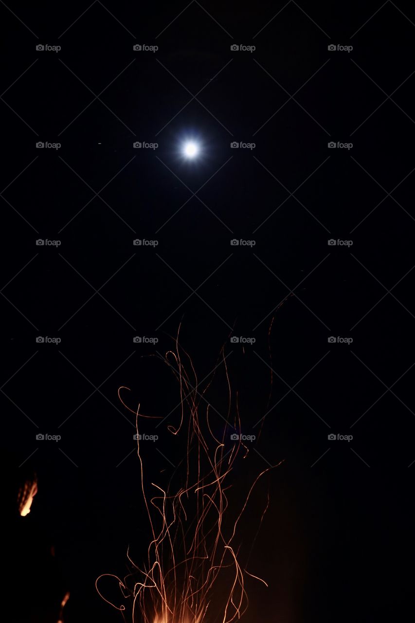 A full moon shining over a campfire in the wilderness at night.