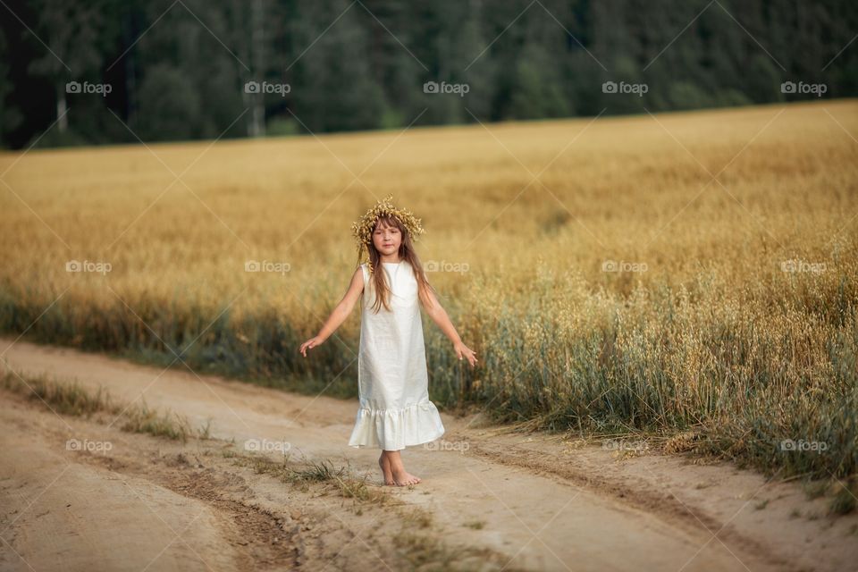 Girl running on the sand road through the rye field 