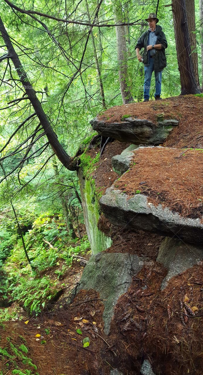 Park Ranger stands atop boulders overlooking the forest valley below; during a hike in early autumn.