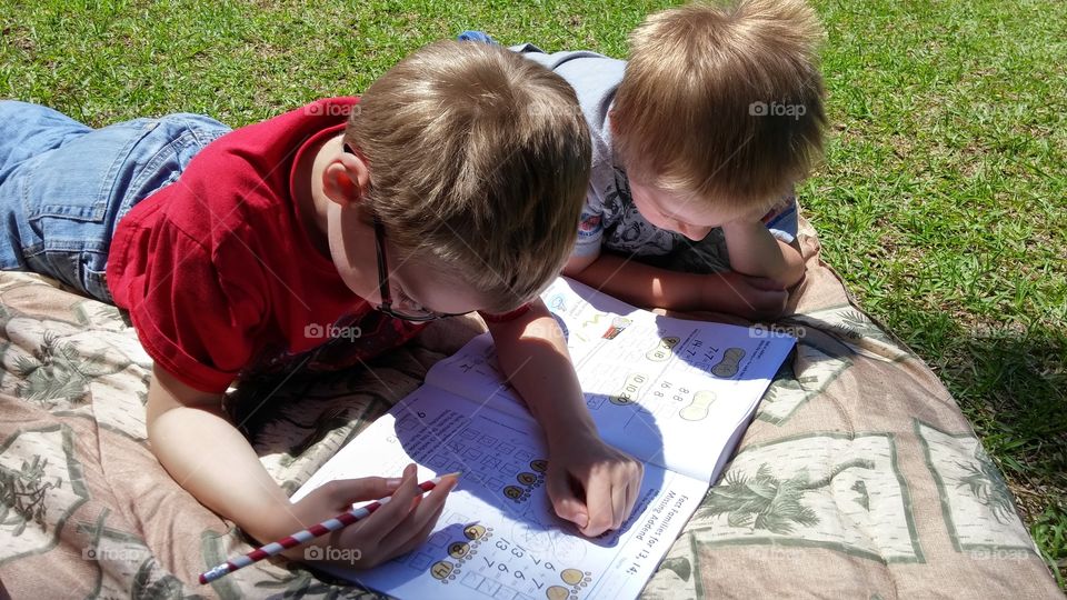 Two boys look at a math workbook during an outdoor home school session.