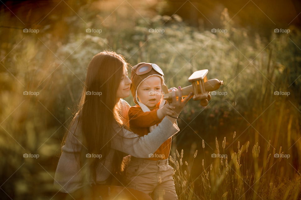 Mother with son playing with wooden plane at sunset