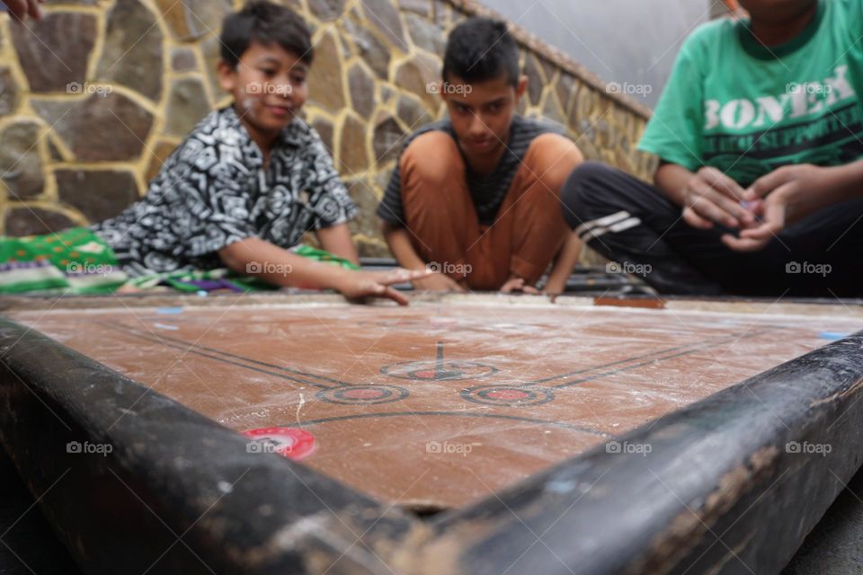 children playing carrom and in the portrait from the end of the carrom game board