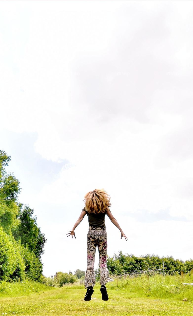 woman jumping in the air with waving hair seen from the back wide angle picture