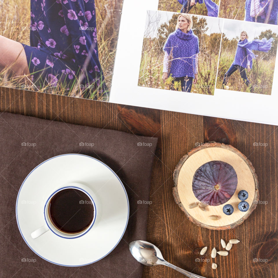 Morning coffee with a fashion magazine.  Food photo, flat lay.  Girl's breakfast: a cup of coffee on a textile napkin on a wooden background with a magazine and a wooden stand with figs, blueberries and seeds