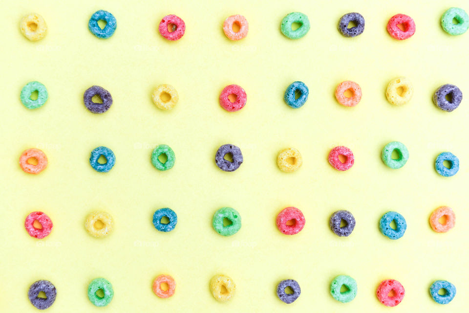 Flat lay of rows of multicolored cereal rings on a yellow background