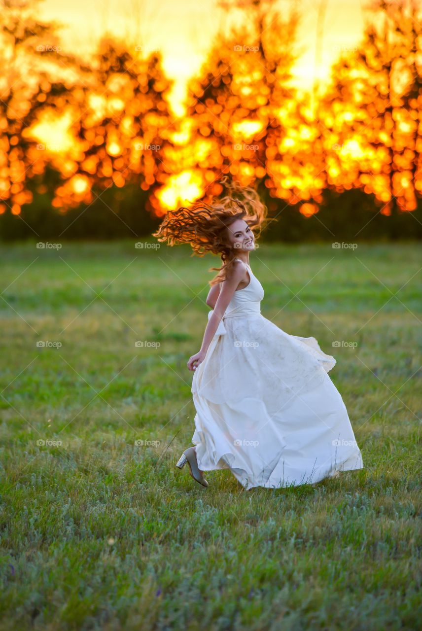 девушка в длинном белом свадебном платье убегает на закате дня в стиле прованс