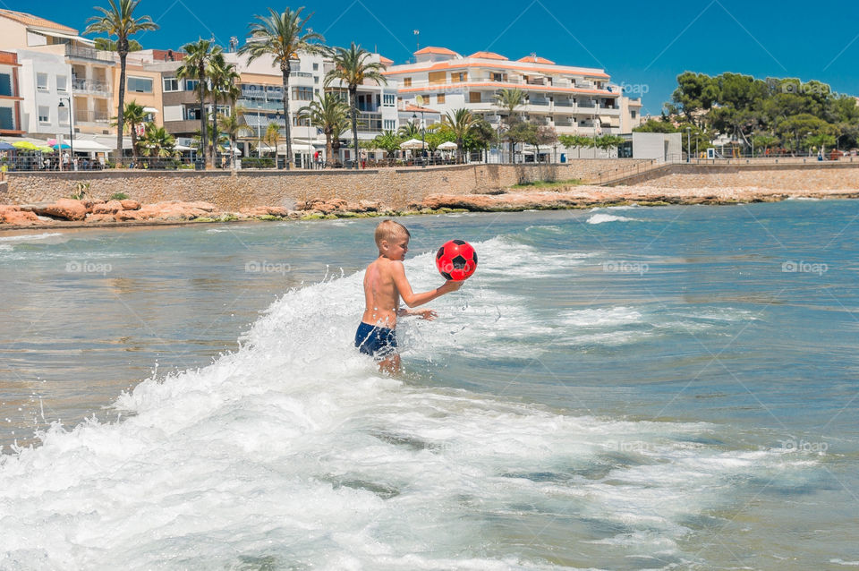 Boy swimming in the sea and playing with red ball