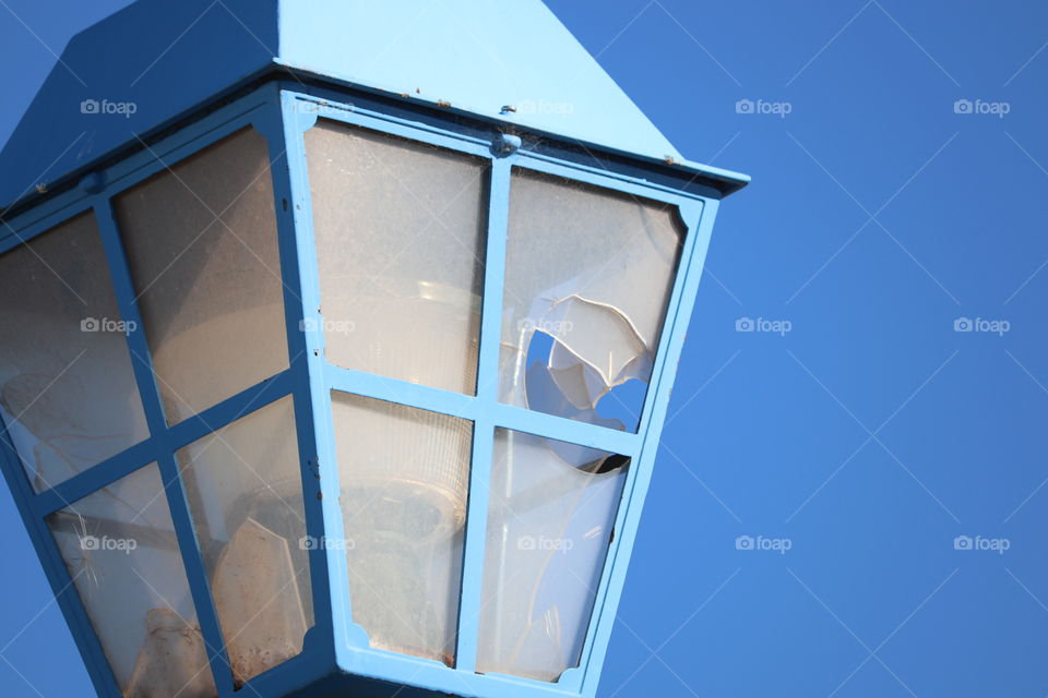 Closeup vintage blue outdoor street lamp with broken glass against a vivid blue sky