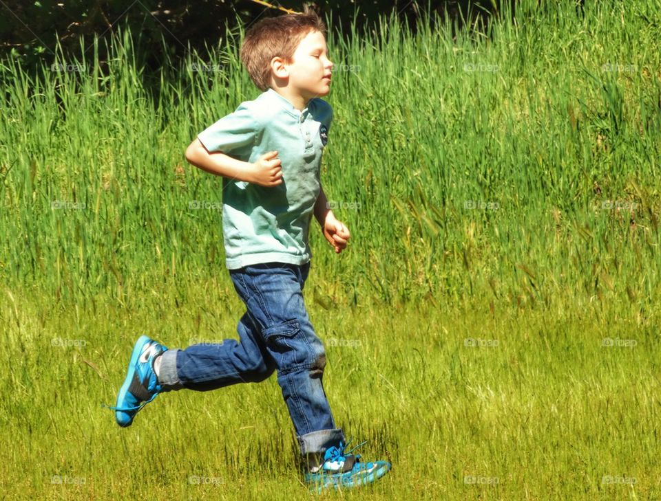 Young Boy Running Through A Green Field
