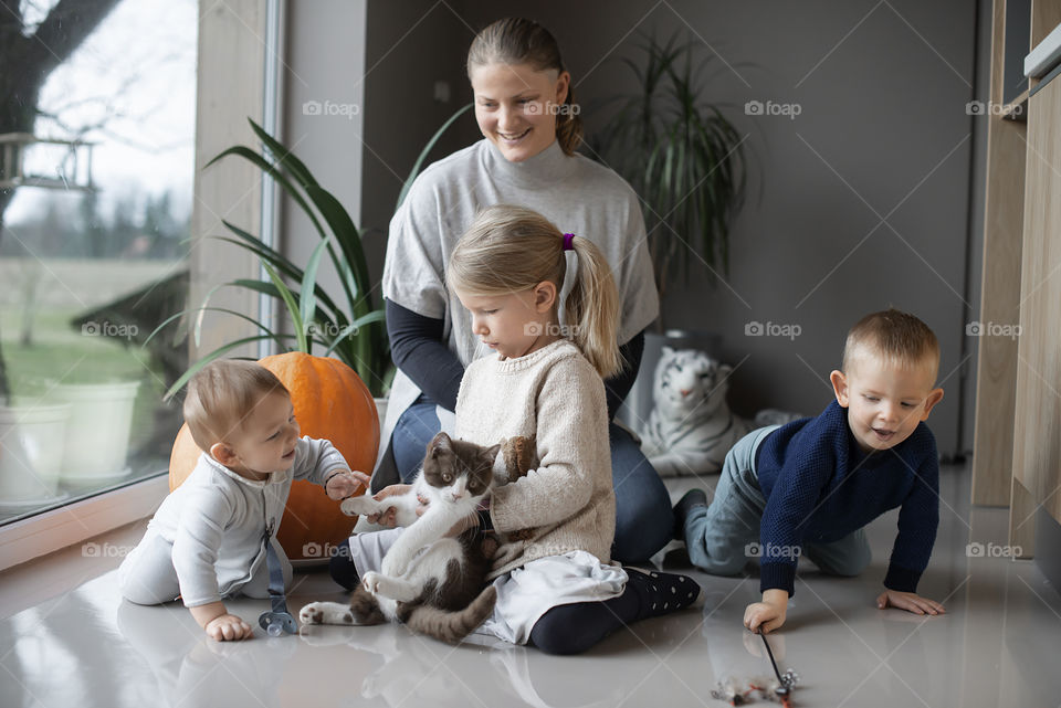 A mother and her three children play with a cat on the floor at home