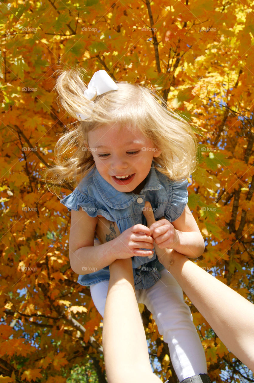 Mother's holding little girl against autumn tree