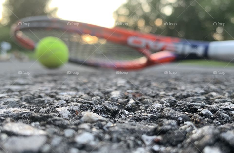 A blurred tennis racket and tennis ball in front of the sun shining through the tennis racket.  