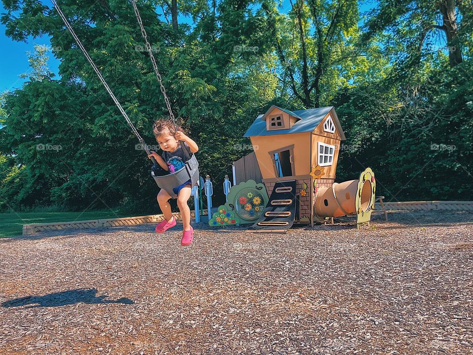 Toddler swinging at playground, child swinging high, small girl at the park swinging