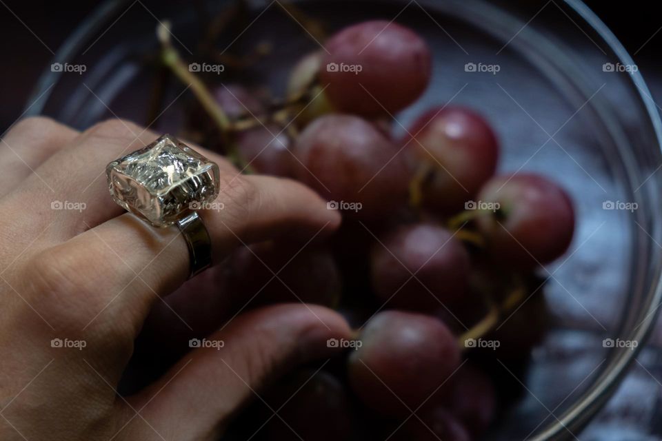 A hand with a sparkling ring takes grapes